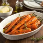 A bowl of perfectly caramelized glazed carrots garnished with fresh thyme.