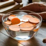 Sweet potato slices soaking in water on a kitchen counter.